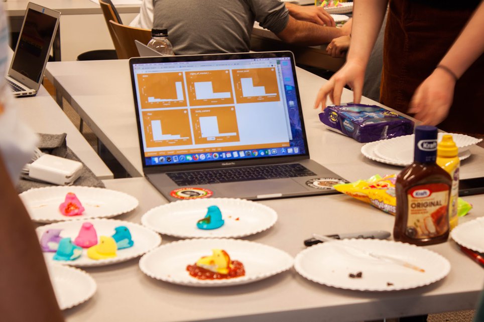 A laptop computer rests on a folding table surrounded by paper plates full of marshmallow peep candies.